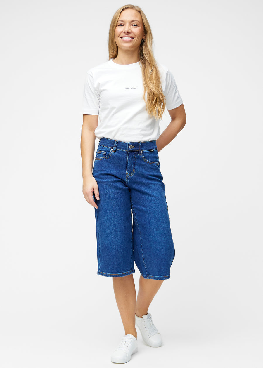 Fuldt billede af model i løse, mørkeblå denim capris i farven Oceans, der går til lige under knæet.