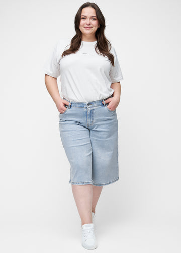 Full image of a plus-size model wearing loose, light blue denim capris in the colour Waves, reaching just below the knee.