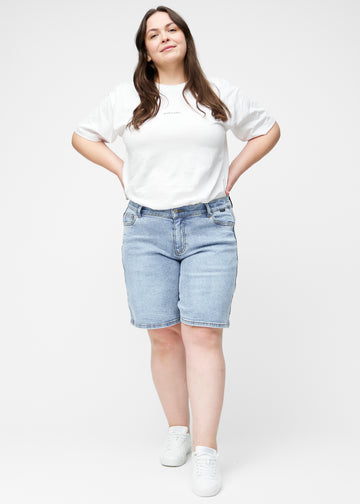 Full image of a plus-size model wearing loose, light blue denim shorts in the colour Waves, reaching just above the knee.