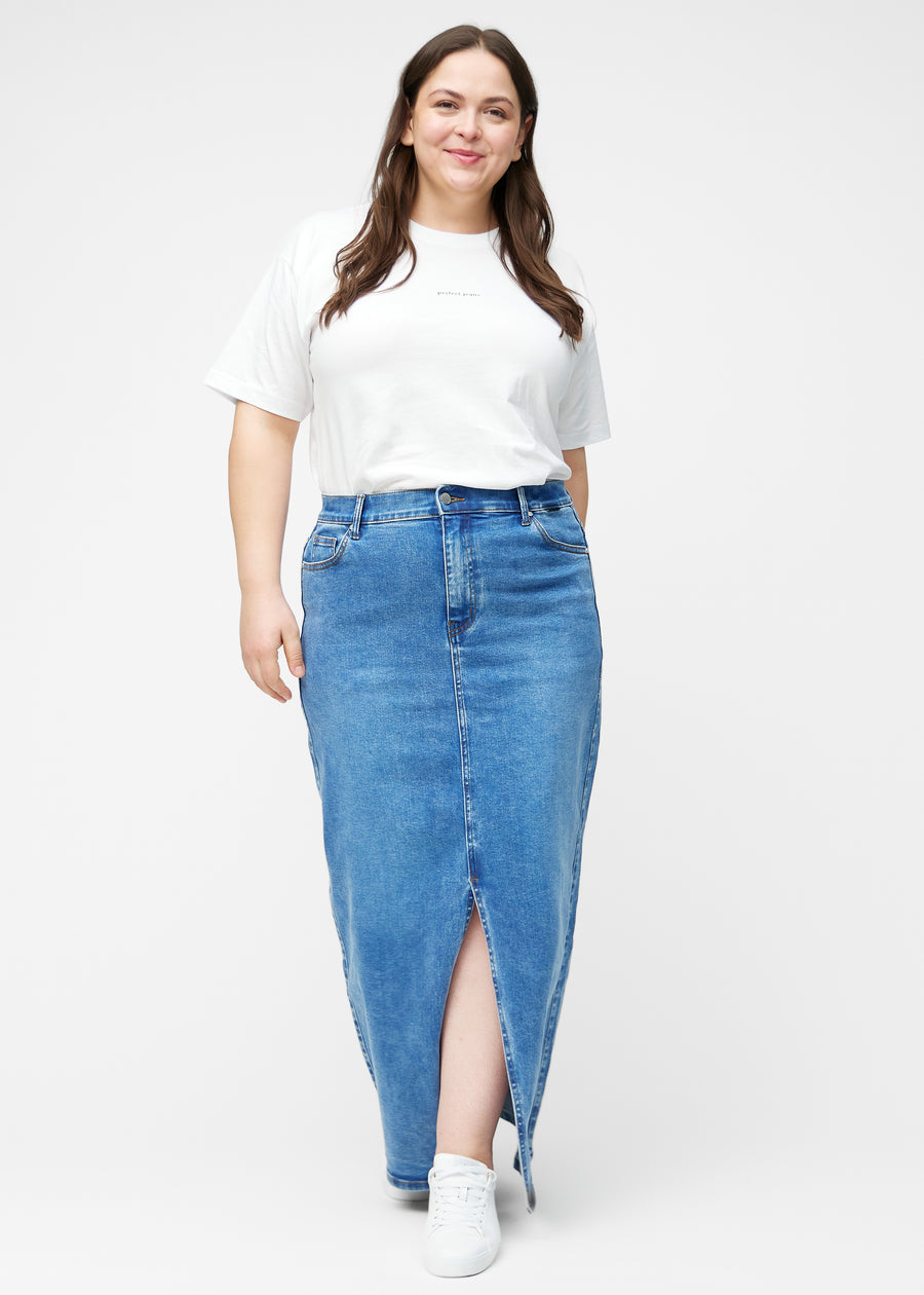 Fuldt billede af plus-size model i lang, klassisk blå denimnederdel i farven Rivers med regulær pasform og slids foran.