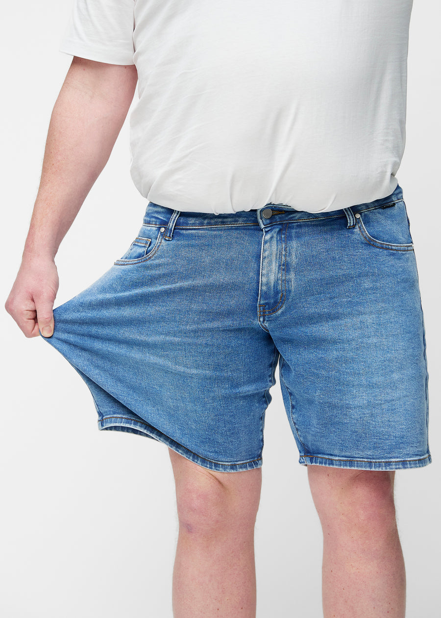 Plus-size model stretches the blue denim shorts for men in the colour Rivers at the thigh to show the stretch of the material.