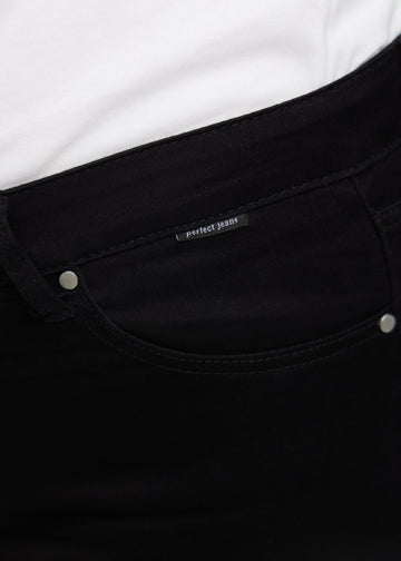Close-up of black jeans material with the Perfect Jeans logo label at the edge of the front pocket on a plus-size model.
