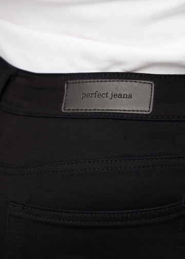 Close-up of black jeans material with the Perfect Jeans leather patch at the back of the waistband on a plus-size model.