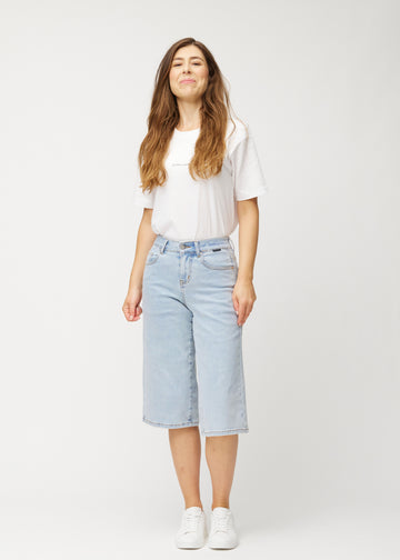 Full-length view of a model wearing loose, light blue Waves denim capris that end just below the knee.