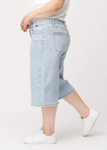 Side view of loose, light blue Waves denim capris on a plus-size model, showing the wide fit and length to just below the knee.