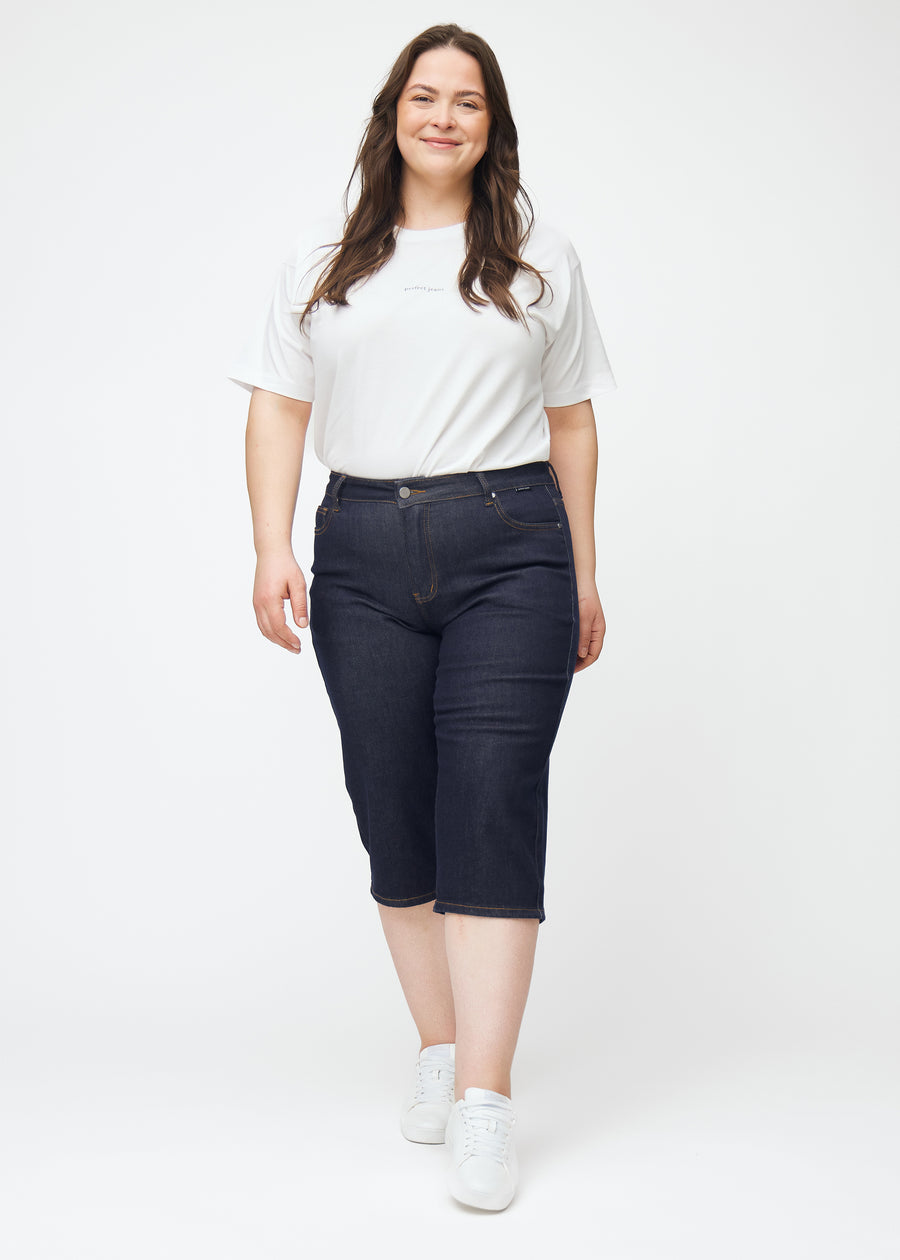 Full image of a plus-size model wearing deep dark blue denim capris for women in the colour Midnights with a regular fit.