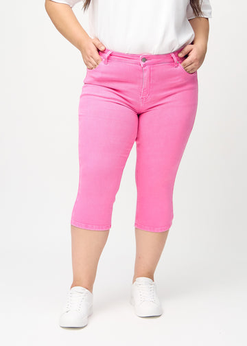 Skinny capris for women in pastel pink fabric, color Flamingos. Front view on a plus-size model, showing the close-fitting legs ending just below the knee.