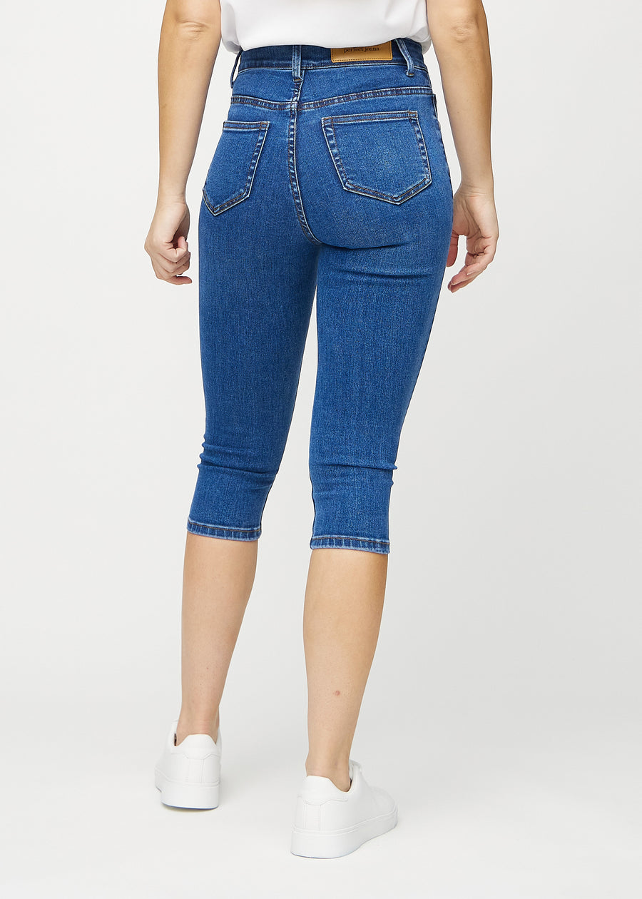 Skinny capris for women in dark blue denim, color Oceans. Back view on a model, showing the fit and back pockets.