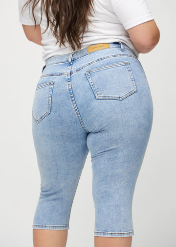 Skinny capris for women in light blue denim, color Waves. Close-up from behind on a plus-size model, highlighting pockets and stitching.