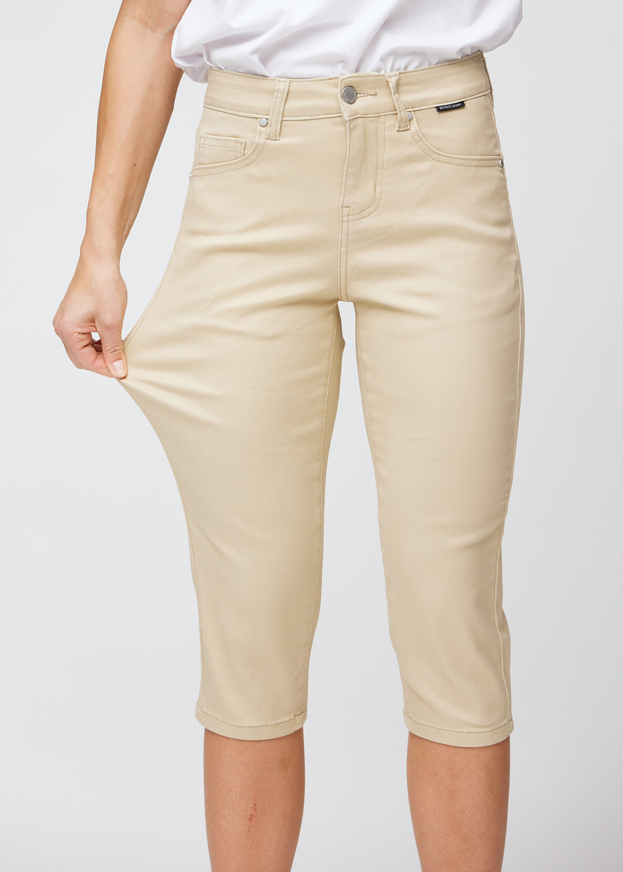 Slim capris for women in beige jeans fabric, color Gazelles. A model pulls the fabric at the thigh to demonstrate stretch and flexibility.