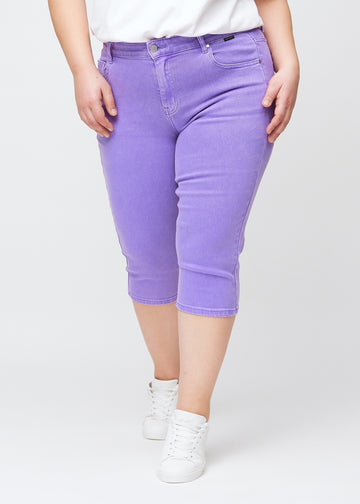 Slim capris for women in pastel purple jeans fabric, color Lavenders. Front view on a plus-size model, showing the fitted cut ending just below the knee.