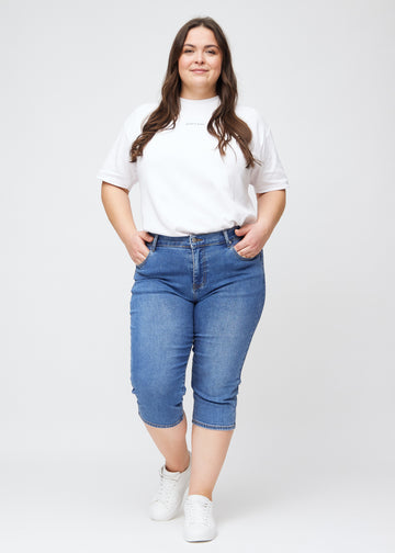Slim capris for women in blue denim, color Rivers. Full-length view of a plus-size model wearing slim capris.