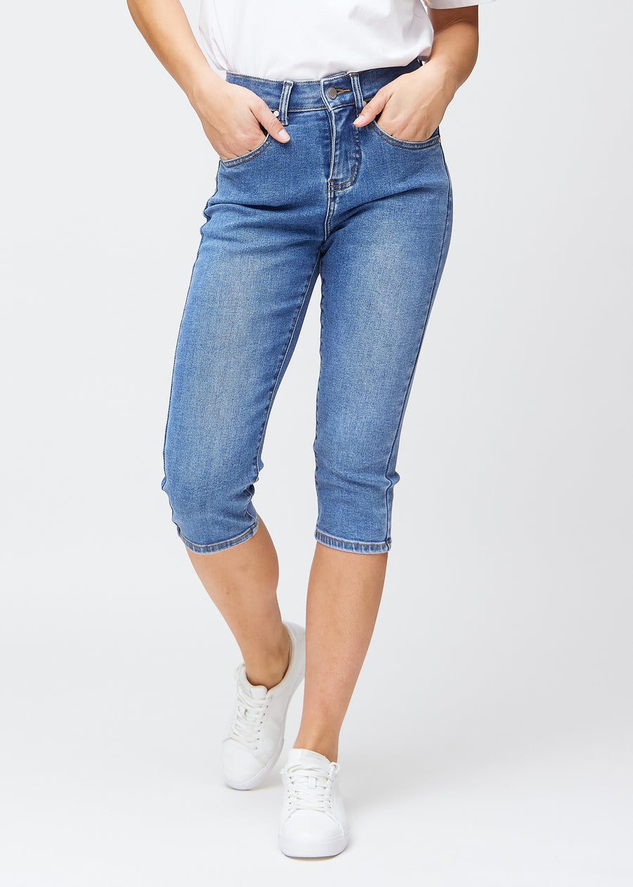 Slim capris for women in blue denim, color Rivers. Front view on a model, showing the fitted cut ending just below the knee.