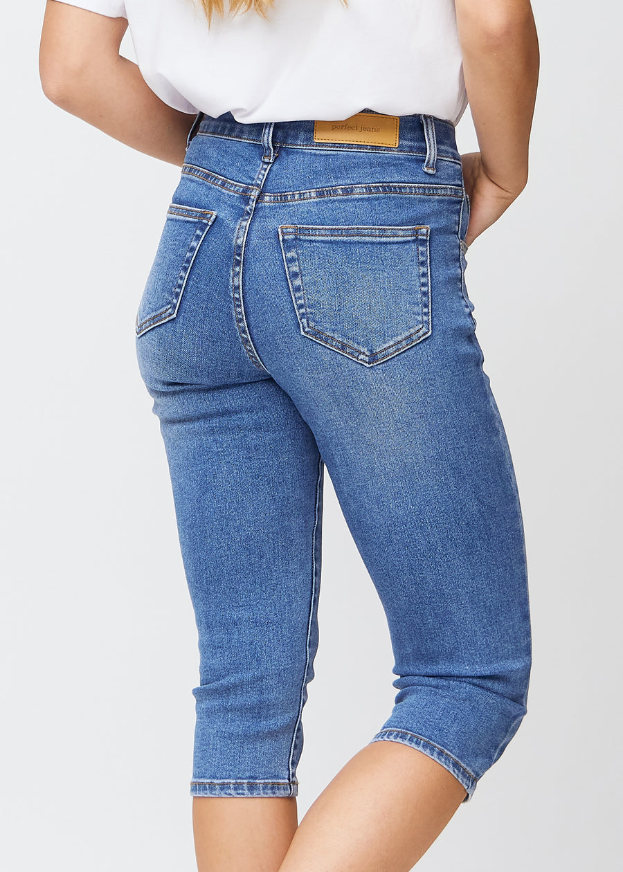 Slim capris for women in blue denim, color Rivers. Close-up from behind on a model, highlighting the back pockets and stitching.