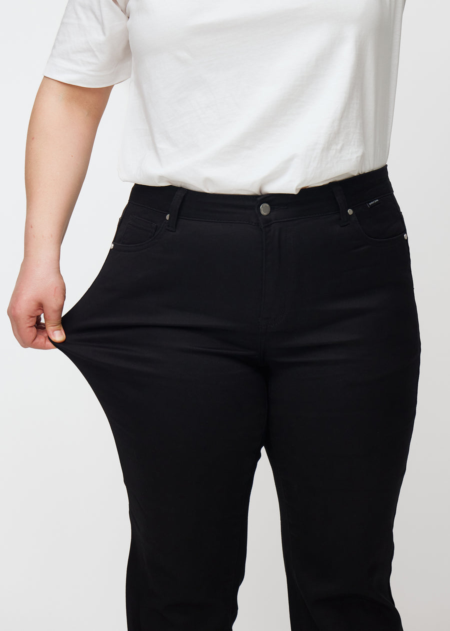 Plus-size model strækker jeansene ved låret for at vise stretch.
