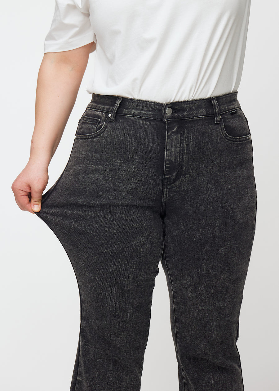 Dark grey mid-rise bootcut jeans in Shadows. A plus-size model stretches the jeans at the thigh to show the fabric&
