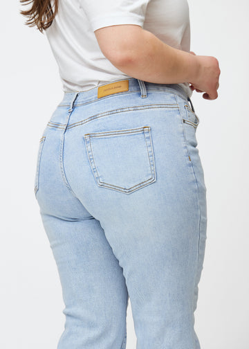 Light blue mid-rise bootcut jeans in Waves. Close-up back view on a plus-size model, showing the details.
