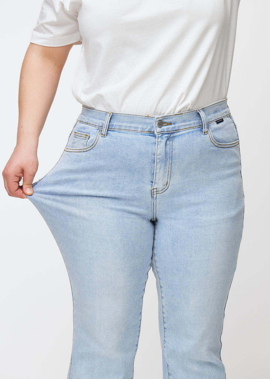 Light blue mid-rise bootcut jeans in Waves. A plus-size model stretches the jeans at the thigh to show the fabric&