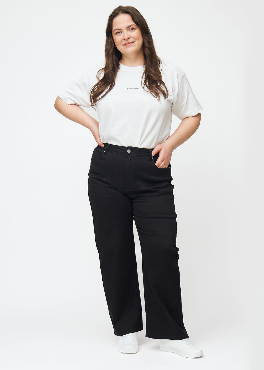 A full image of a plus-size model in black high-waisted jeans, which are fitted at the waist and have a loose fit with width down the leg.