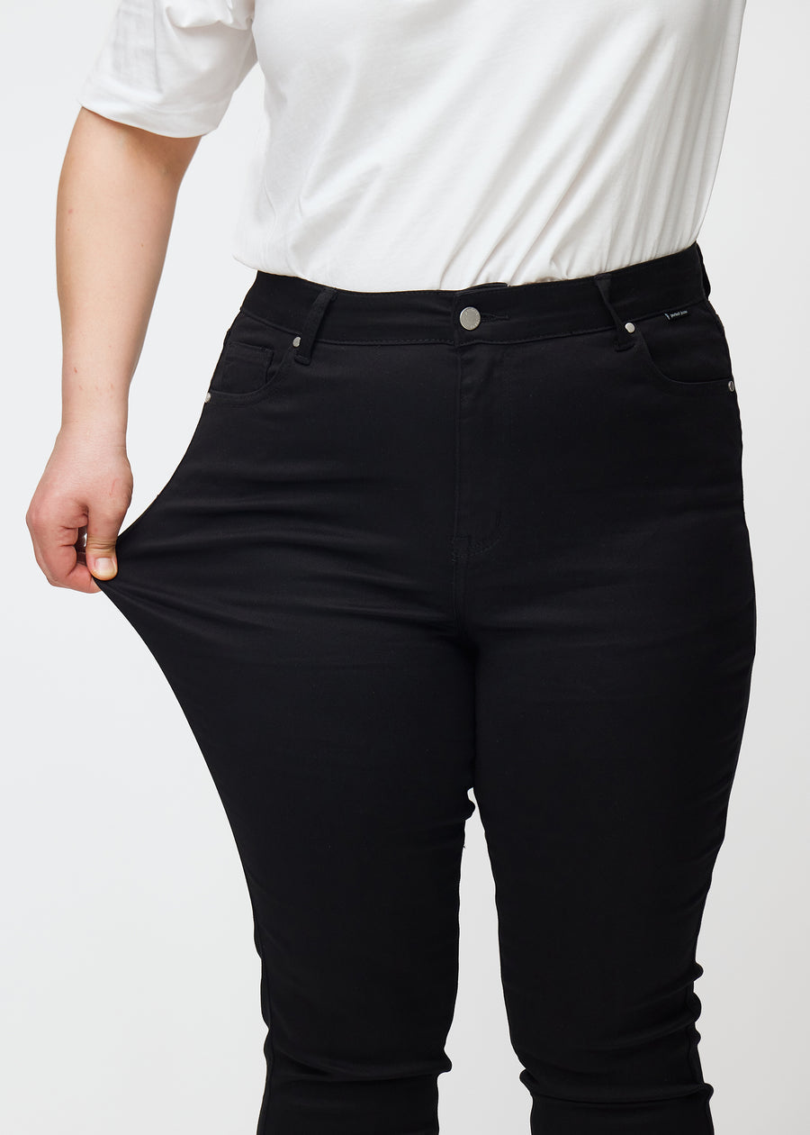 A plus size model stretches the black stretch jeans with a high waist in the color Ravens.