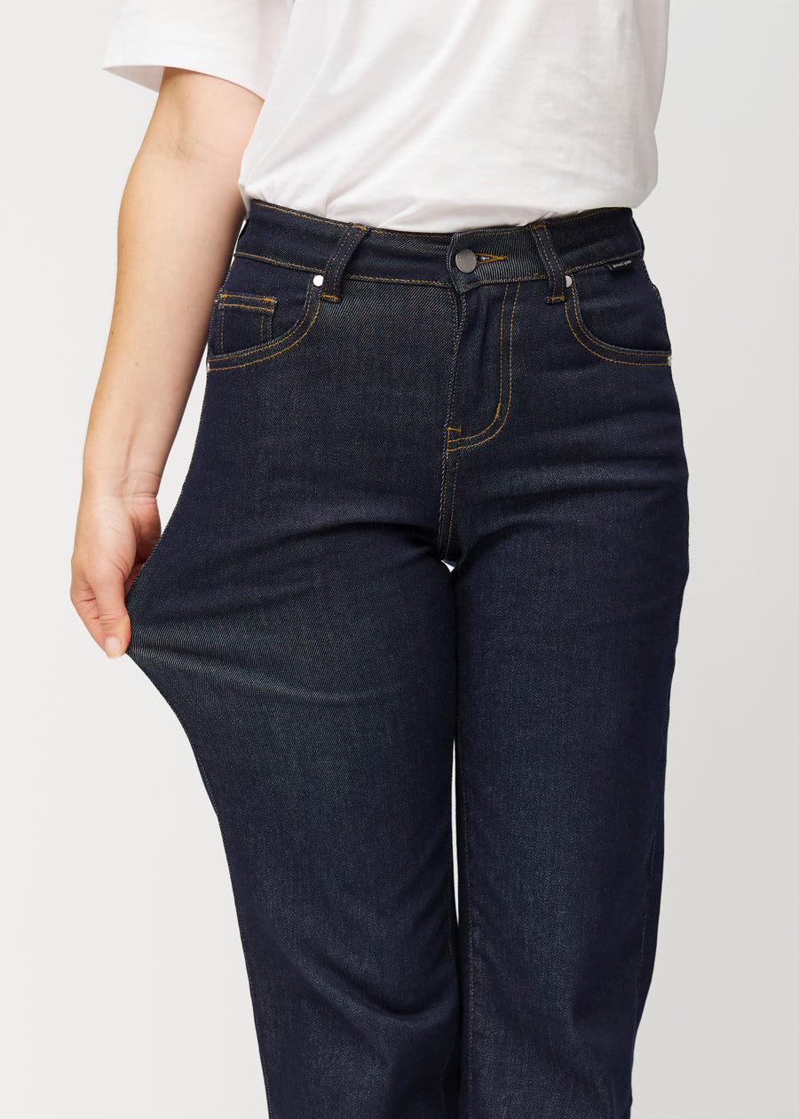 The model stretches the deep dark blue denim jeans for women in the colour Midnights at the thigh to show the stretch of the material.