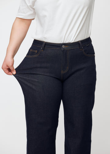 Plus-size model stretches the deep dark blue denim jeans for women in the color Midnights at the thigh to show the material&