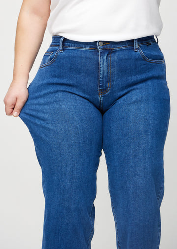 Loose jeans for women in dark blue, color Oceans. A plus-size model stretches the denim at the thigh to show the fabric&
