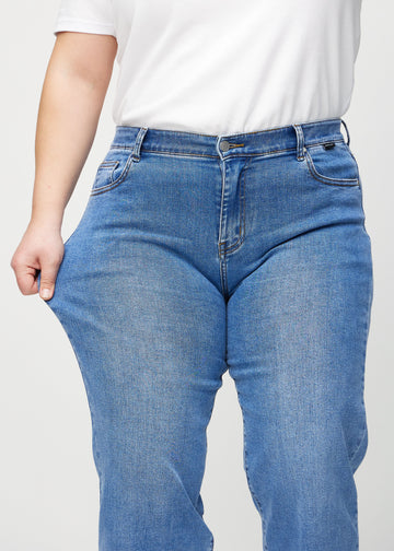 The plus-size model stretches the jeans at the thigh to show the stretch.
