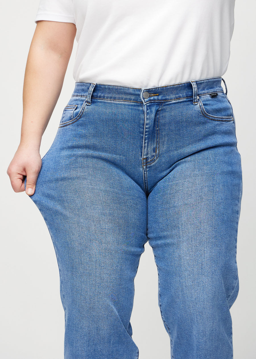 The plus-size model stretches the jeans at the thigh to show the stretch.