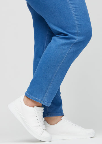 Regular jeans for women in blue, color Geraniums. Close-up at the ankles on a plus-size model, showing the straight leg openings.
