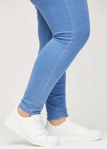 Skinny jeans for women in blue, color Geraniums. Close-up at the ankles on a plus-size model, showing the close-fitting leg openings.