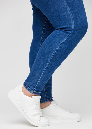 Skinny jeans for women in dark blue, color Oceans. Close-up of the snug-fitting leg openings at the ankles on a plus-size model.