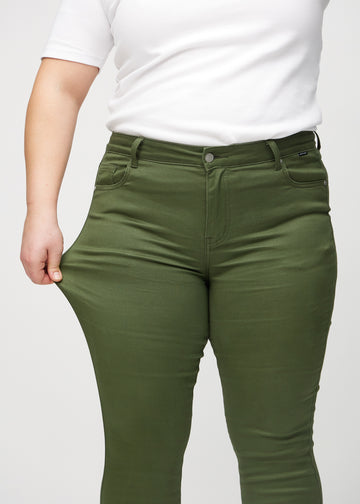 Skinny jeans for women in dark green, color Renewals. A plus-size model stretches the jeans at the thigh to show the fabric&