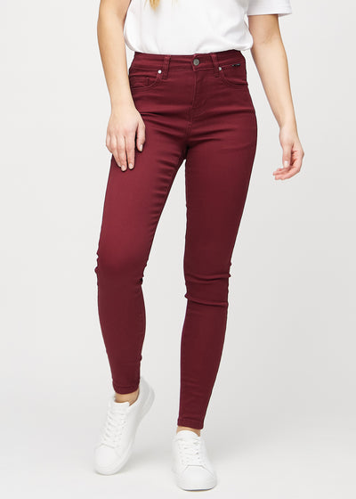 Skinny jeans for women in dark red, color Santas. Front view on a model, showing the close fit through the legs.