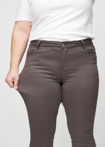 Skinny jeans for women in grey brown, color Thunders. A plus-size model stretches the jeans at the thigh to show the fabric&