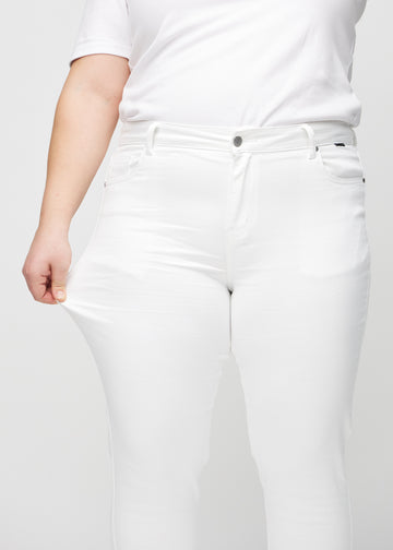 Slim jeans for women in white, color Marguerites. A plus-size model stretches the jeans at the thigh to show the fabric&