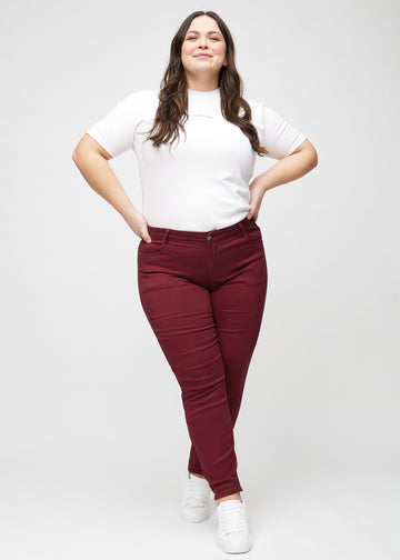 Slim jeans for women in dark red, color Santas. Full-length view of a plus-size model wearing the jeans.