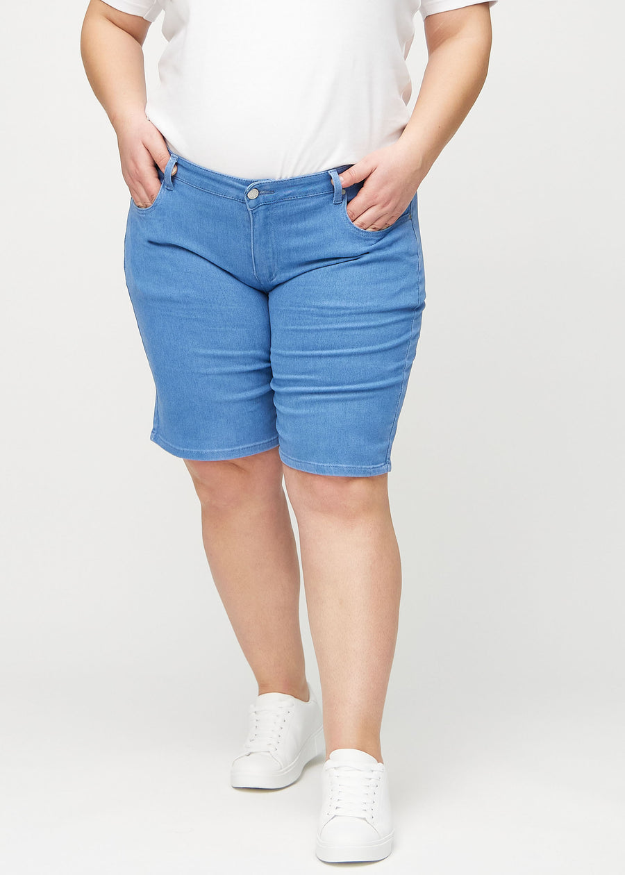 Blue regular middle shorts, model name Geraniums, which go straight down the leg and end just above the knee on a plus-size model, seen from the front.