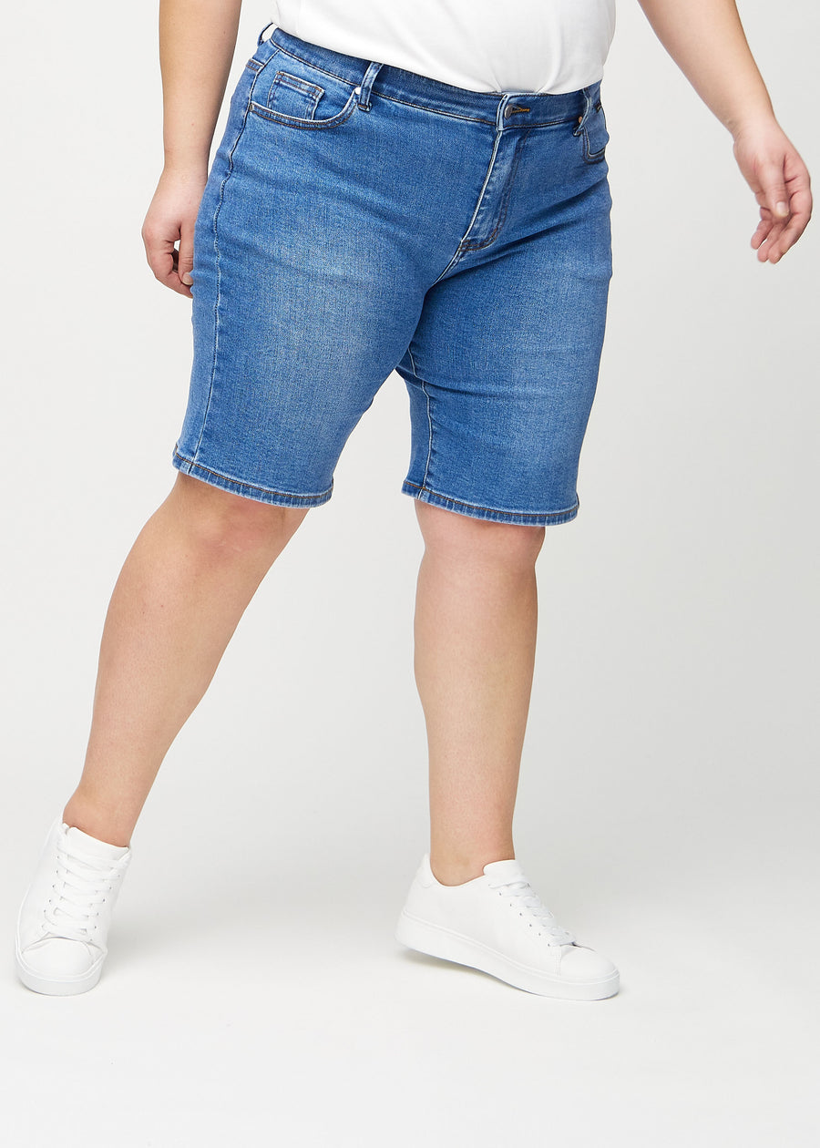 Denim regular middle shorts, model name Rivers, which fall straight down the leg and end just above the knee on a plus-size model, seen from the front.