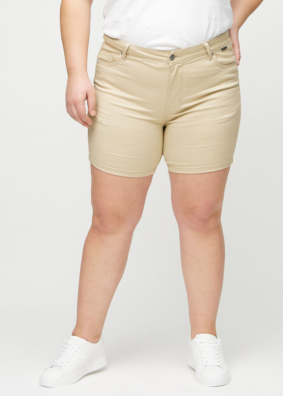 Beige skinny short shorts, model name Gazelles, with a close fit and ending mid-thigh on a plus-size model, seen from the front.