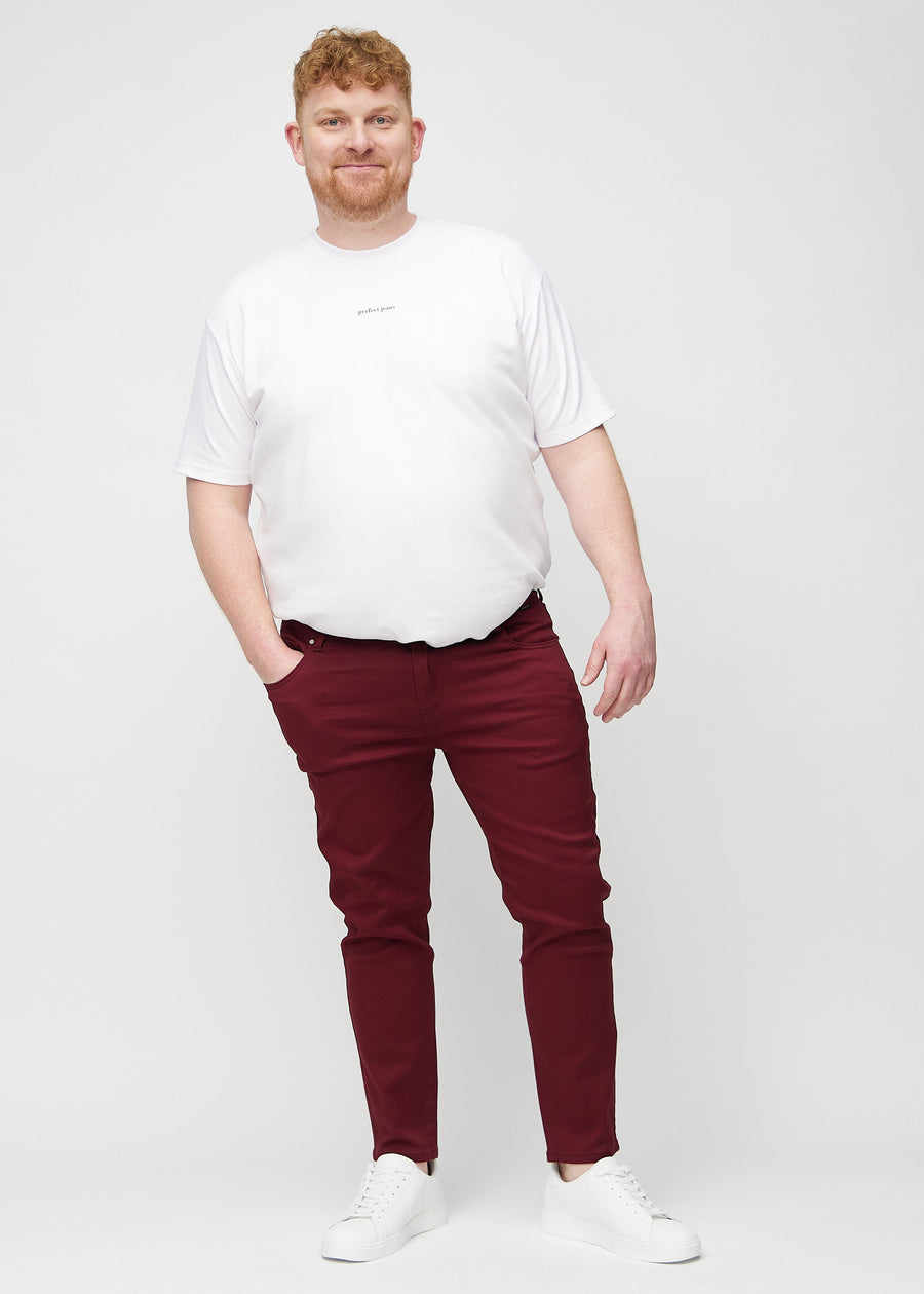 Full-length view of a plus-size model in dark red slim jeans.