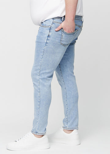 Light blue denim slim jeans viewed from the side on a plus-size model.