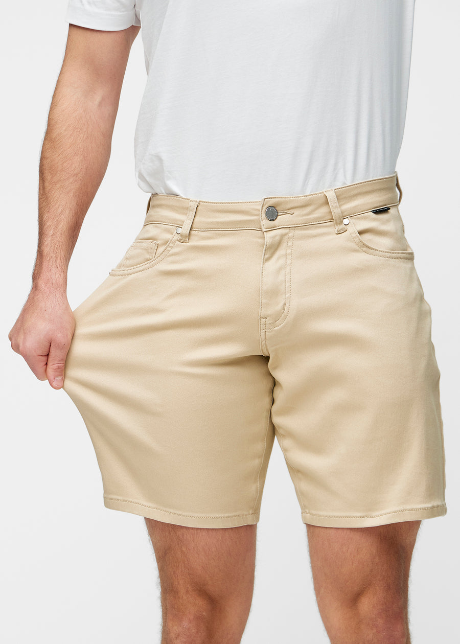 Model stretches the beige shorts for men in the colour Gazelles at the thigh to show the stretch of the material.