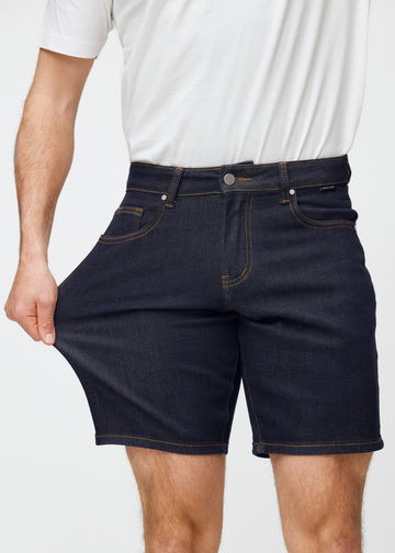 model stretches deep dark blue denim shorts for men in the colour midnights at the thigh to show the material’s stretch.
