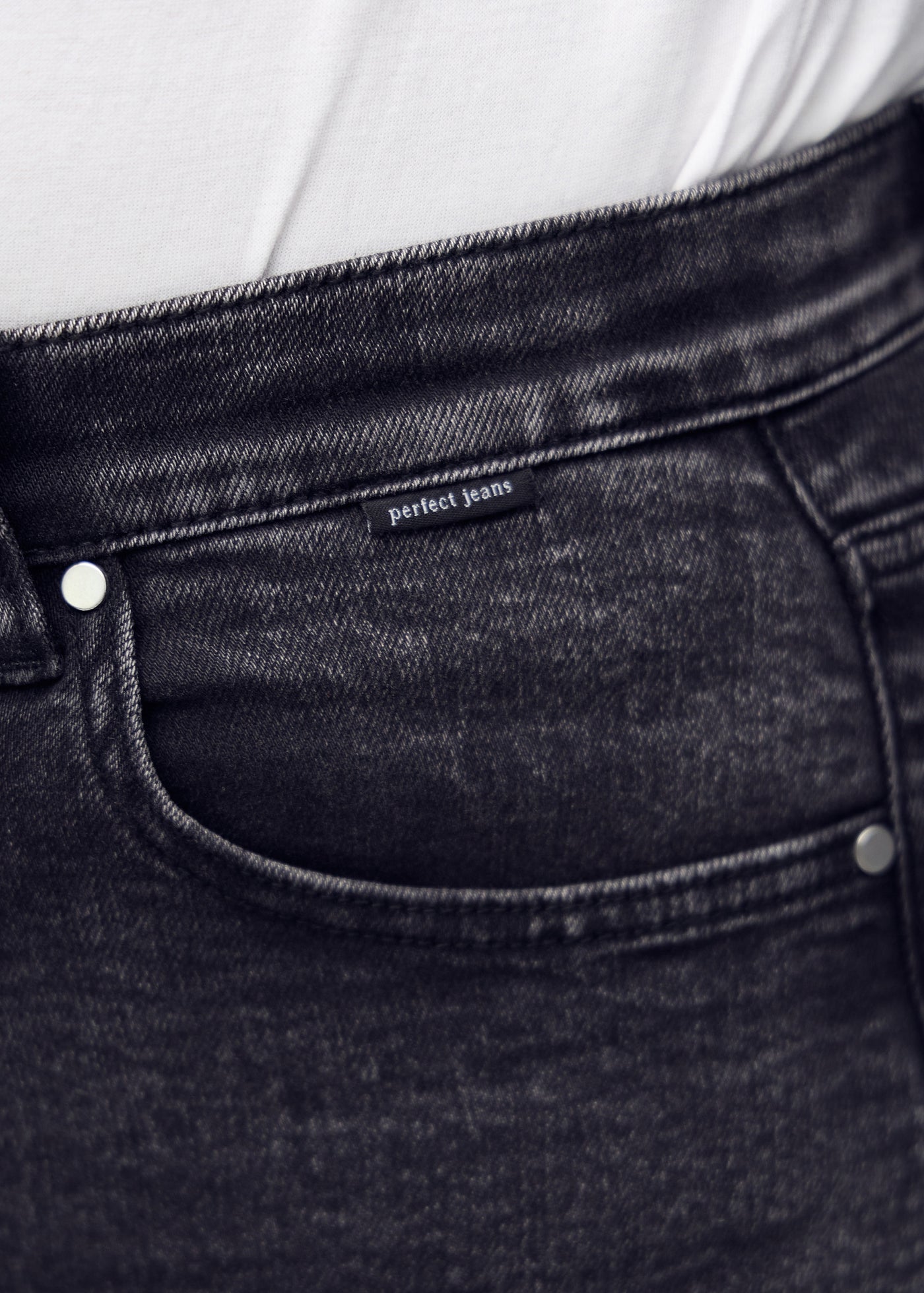 Detaljebillede af forlommen på den mørkegrå denim i farven Shadows – logo og snit fremhævet på plus-size model.