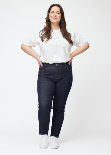 Plus-size model viser dyb mørkeblå denim jeans til kvinder i farven Midnights med slim pasform i bevægelse.