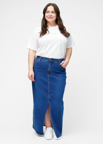 Plus-size model viser lang, mørkeblå denimnederdel i farven Oceans med regulær pasform i bevægelse og demonstrerer slids og materiale.