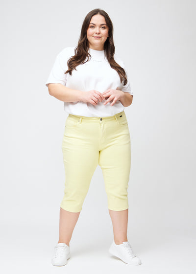 Plus-size model går ind i billedet, strækker i sine lysegule slim capris, drejer rundt for at vise dem frem og forlader derefter billedet.